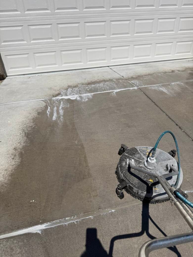 Concrete apron in front of a white garage door being cleaned, showing a sharp clean line