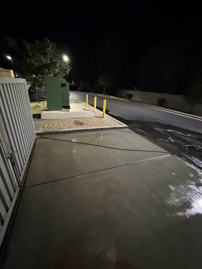 Cleaned concrete approach to a commercial dumpster enclosure at night with yellow bollards