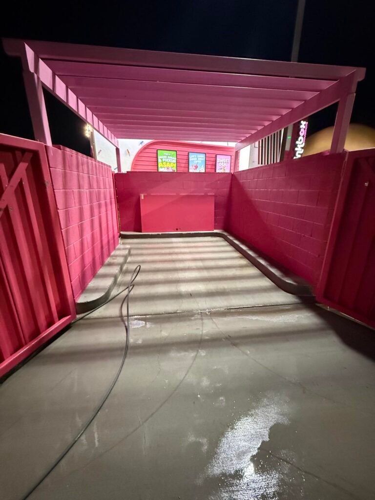 Cleaned concrete dumpster pad inside a painted trash enclosure
