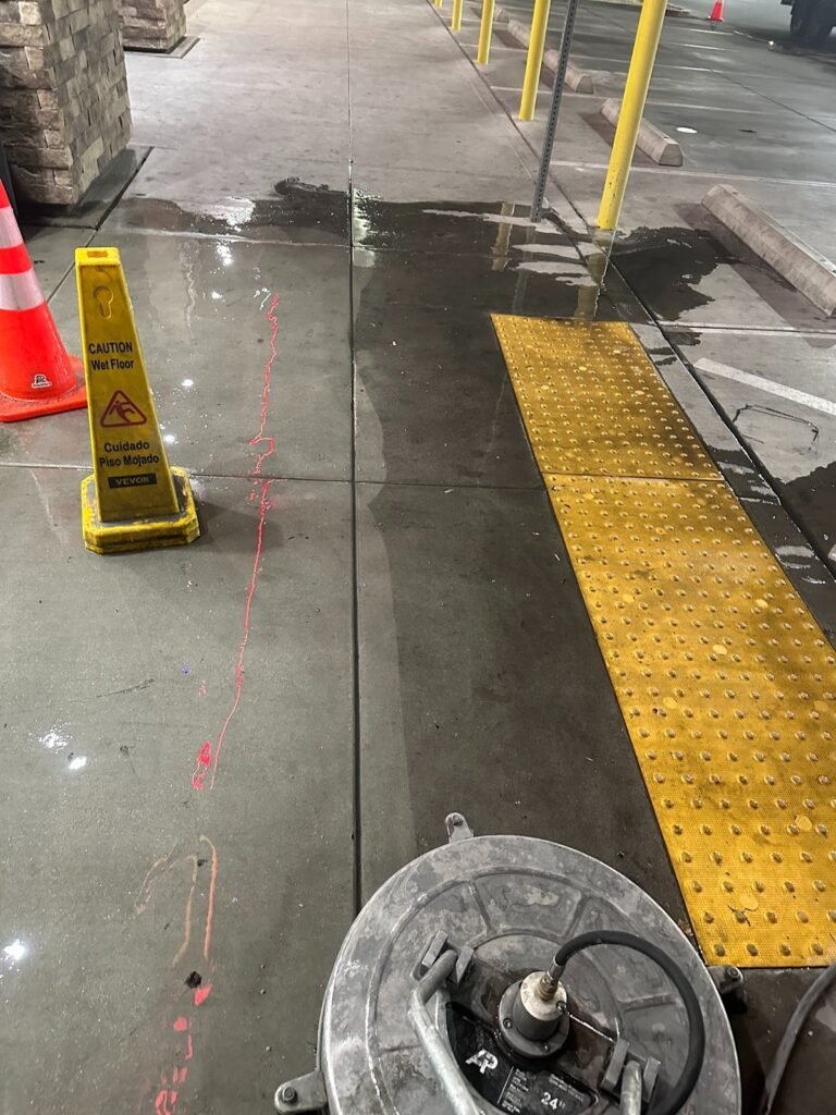 Freshly cleaned sidewalk beside fuel island bollards with a wet floor sign in place