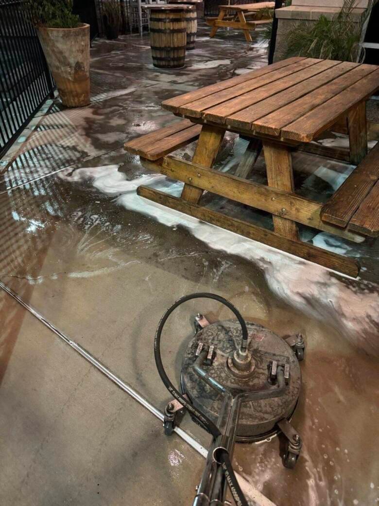 Rotary surface cleaner and detergent foam on a restaurant patio beside wooden picnic tables