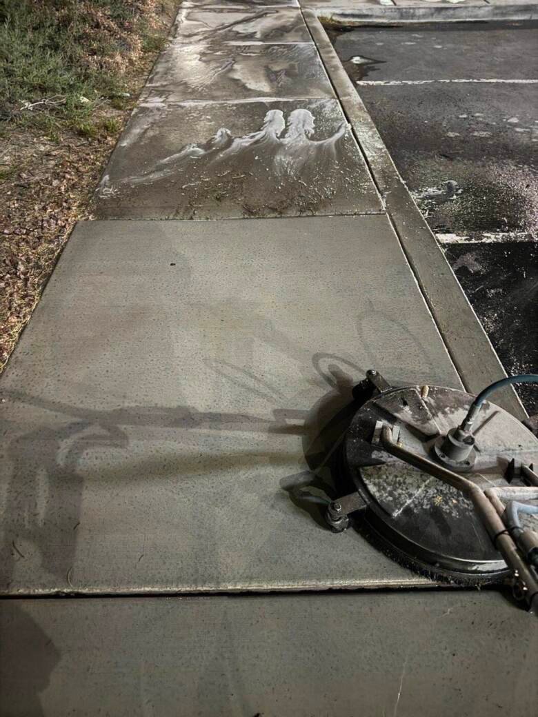Public sidewalk being pressure washed at night with a rotary surface cleaner